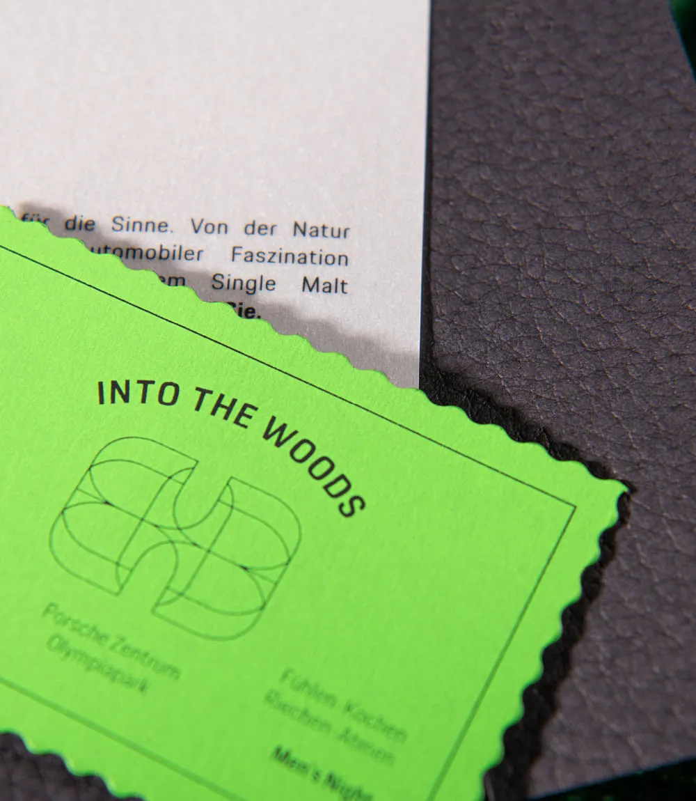 Auf schwarzem Leder liegt ein weißes Blatt Papier mit Text und schräg darüber im Vordergrund angeordnet liegt ein grünes Eintrittsticket für INTO THE WOODS.
