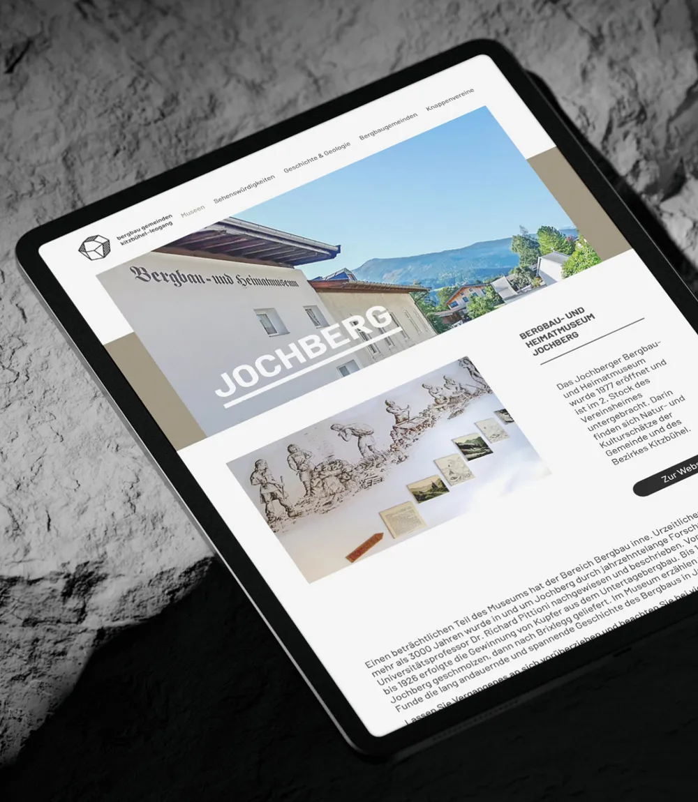 Auf felsigem Hintergrund sieht man ein Tablet mit einem Abschnitt zu Jochberg auf der Website Bergbau Gemeinden Kitzbühel-Leogang.