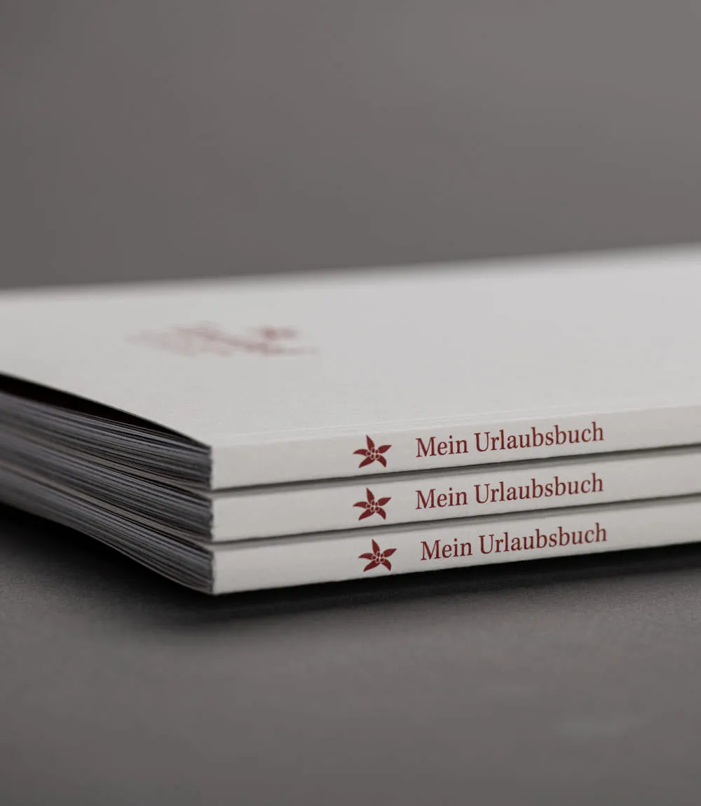 Drei gestapelte weiße Broschüren mit dem Titel 'Mein Urlaubsbuch'.