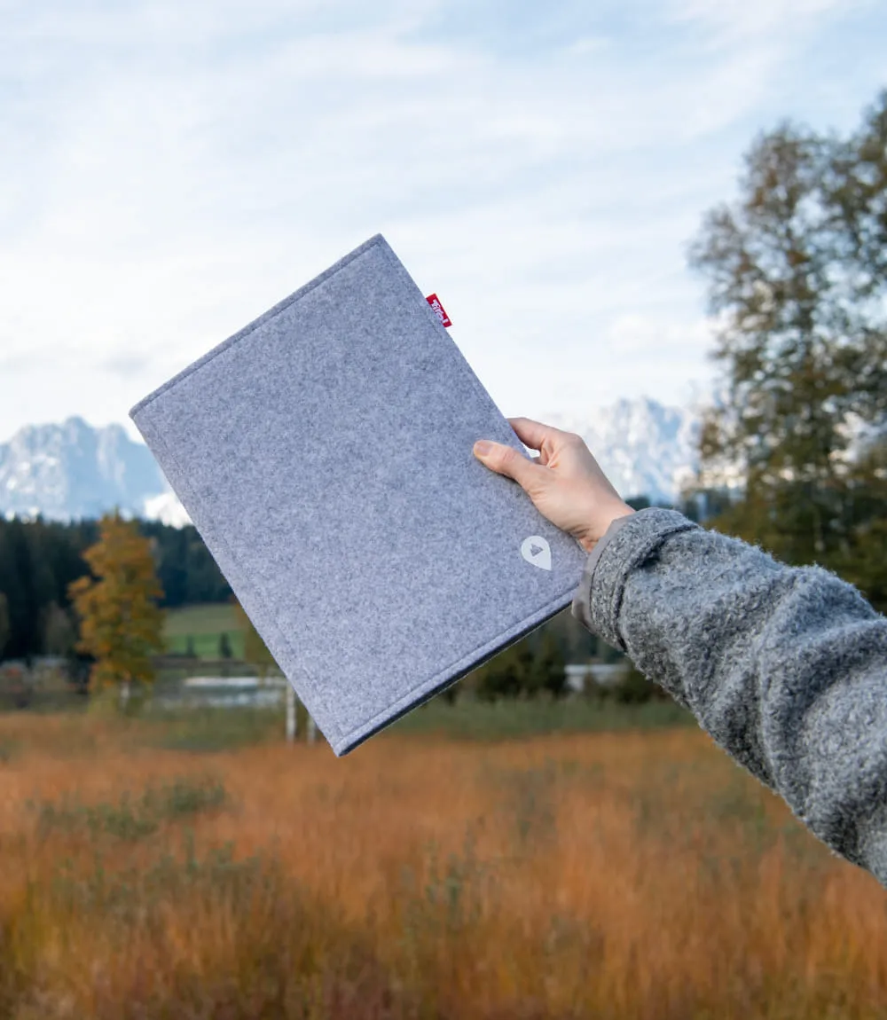 Gezeigt wird rechter Arm einer grau gekleideten Person auf einer Wiese stehend, die eine geschlossene Willkommen in Tirol Mappe hält.
