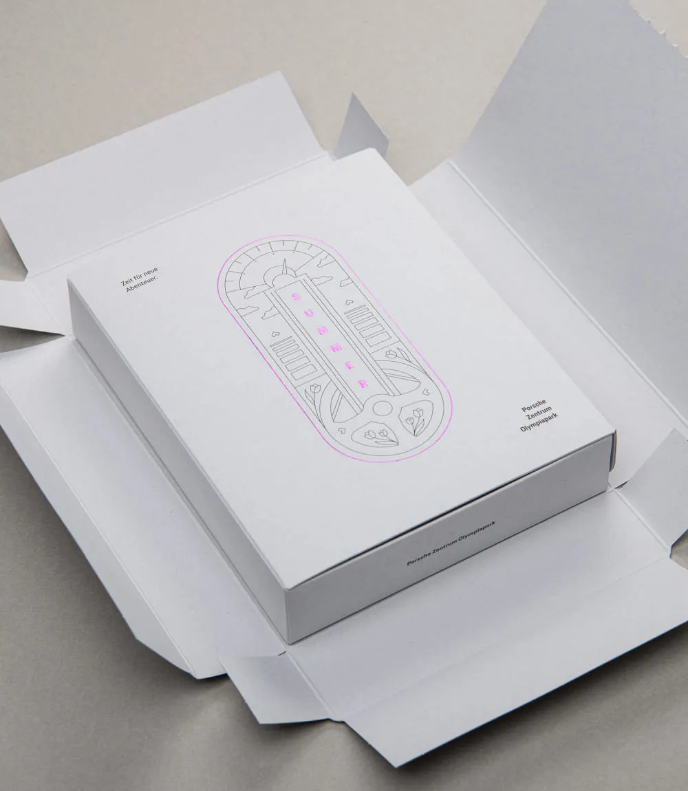 Geöffneter Versandkarton mit Mailingbox des Porsche Zentrums Olympiapark; darauf Illustration mit pinker Prägung SUMMER und der Text Zeit für neue Abenteuer.