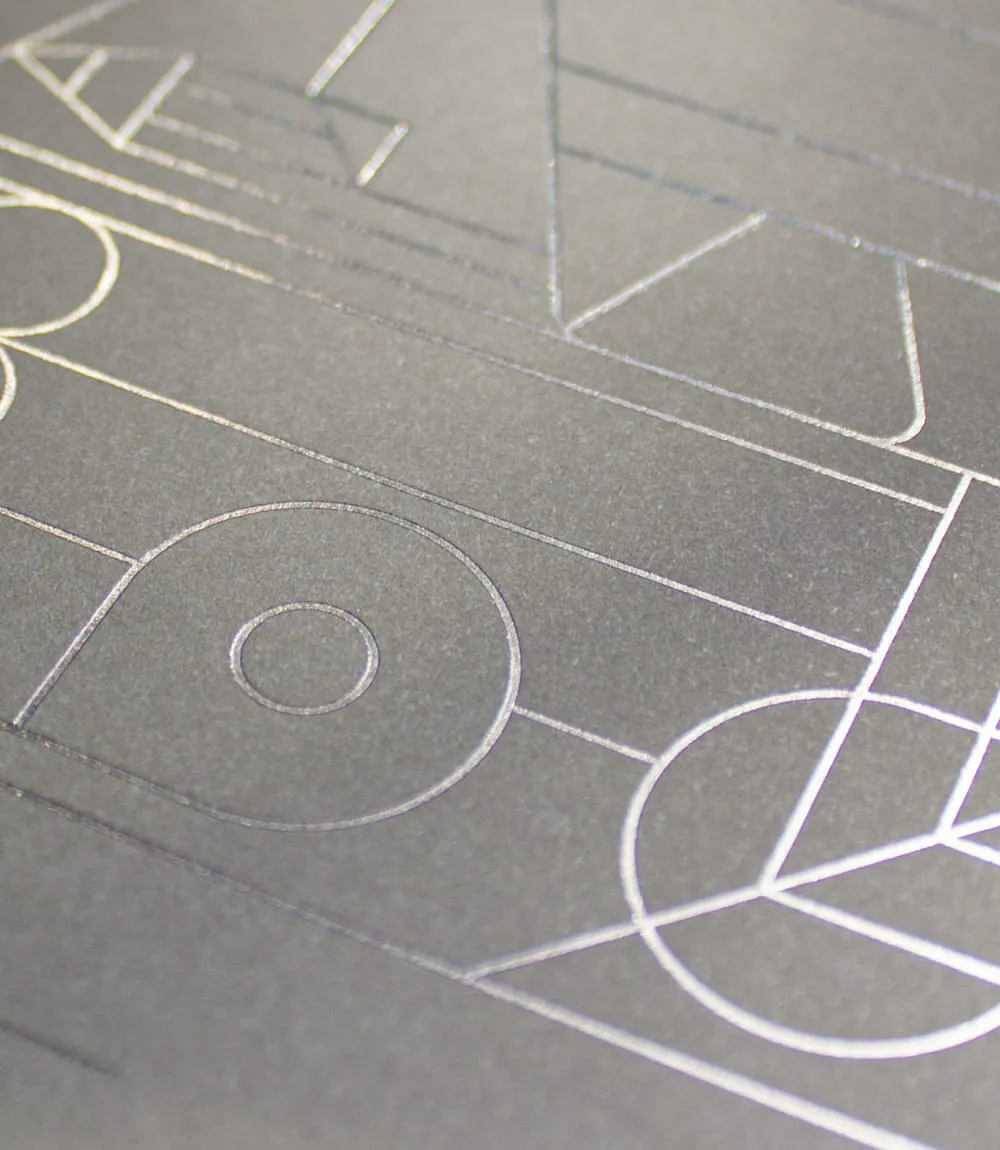 Detailaufnahme eines geprägten Covers mit filigranen Linien und geometrischen Formen in schimmernder Metallicfolie auf grauem Feinstpapier.