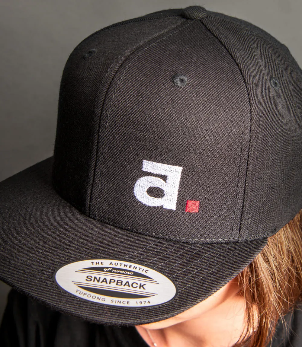 Person von oben fotografiert trägt schwarze Yupoong Baseball Mütze mit Aschaber Logo.